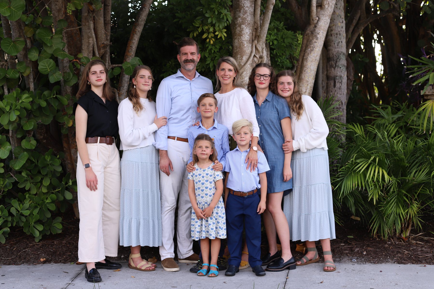 Nicole, Bobby and their children standing together in front of green foliage in Naples