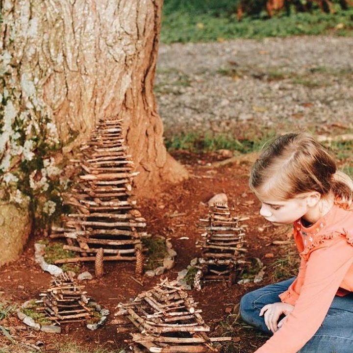 A girl building tiny stick fairy houses at the foot of a tree