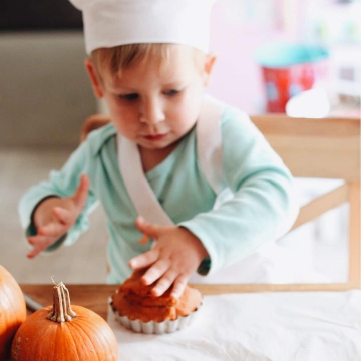 A toddler in a chef hat with a pumpkin muffin